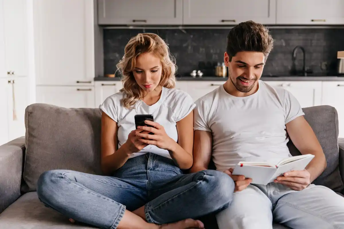 couple sitting on sofa each with phone, one trying to look at other's phone